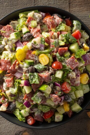Turkey pepperoni grinder chopped salad with romaine lettuce, cucumber, tomatoes, red onion, banana peppers, black olives, provolone cheese, and creamy Italian dressing in a black bowl.