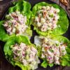 Overhead view of four apple pecan chicken lettuce wraps on a black plate, filled with creamy chicken salad, diced apple, celery, red onion, pecans, and herbs. Fresh apples and pecans sit on a rustic wood table.
