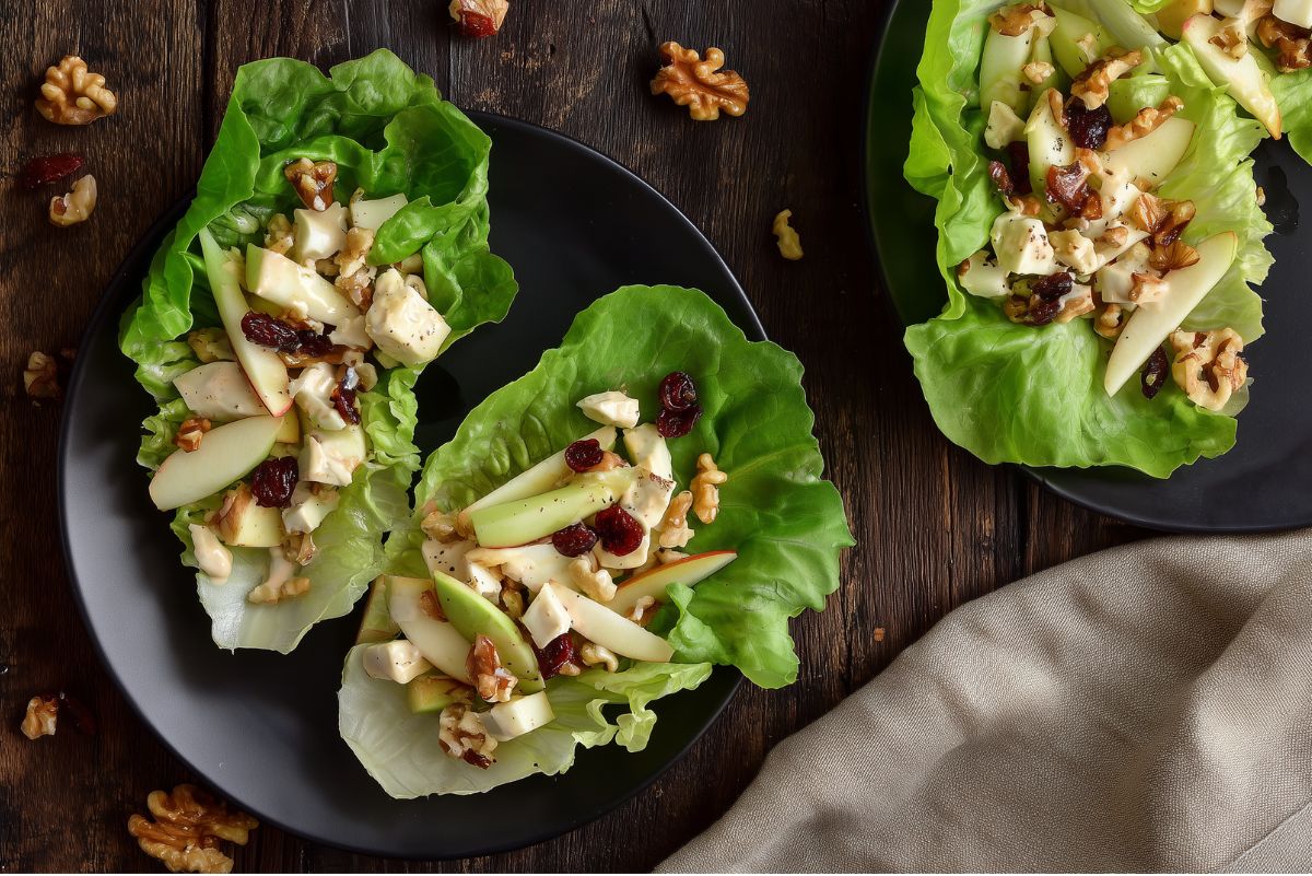 Apple walnut and brie lettuce wraps filled with sliced green apples, brie cheese, walnuts, dried cranberries, and dressing, arranged on black plates over a rustic dark wood table.