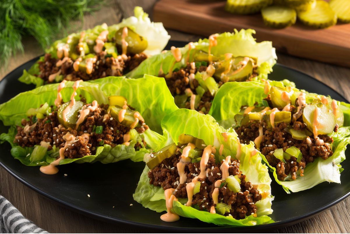 Big Mac lettuce wraps on a black plate with seasoned ground beef, sliced pickles, green onions, sesame seeds, and creamy burger sauce.