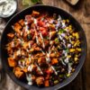 Overhead chicken enchilada sweet potato bowl with roasted sweet potatoes, chicken, black beans, corn, red onion, tomatoes, cilantro, enchilada sauce, and creamy drizzle.