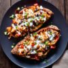 Overhead view of chicken fajita stuffed sweet potatoes filled with shredded chicken, black beans, bell peppers, and green onions, finished with a creamy white sauce on a black plate.