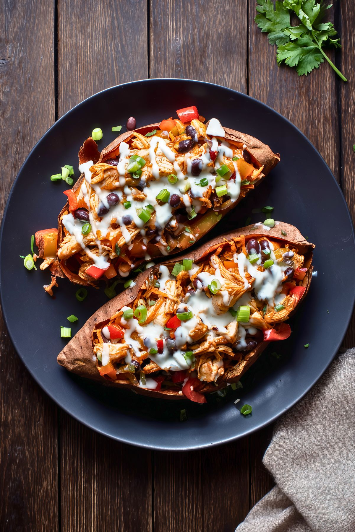 Overhead view of chicken fajita stuffed sweet potatoes filled with shredded chicken, black beans, bell peppers, and green onions, finished with a creamy white sauce on a black plate.
