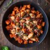 Overhead view of a Chicken Parmesan Sweet Potato Bowl with roasted sweet potato cubes, seasoned chicken, marinara sauce, shredded Parmesan and fresh basil in a black bowl.