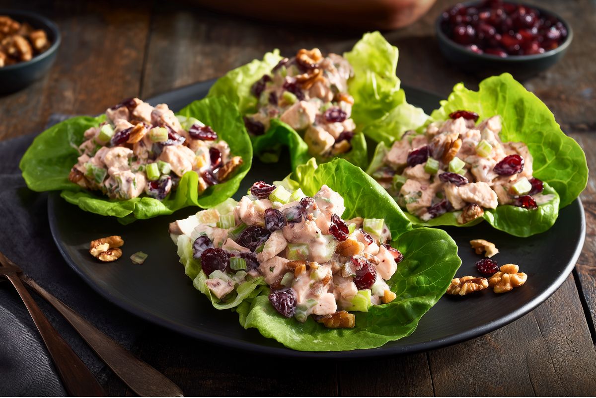 Four Cranberry Walnut Chicken Lettuce Wraps on a black plate, filled with creamy diced chicken, dried cranberries, celery, red onion, and walnuts.