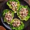 Overhead view of four Cranberry Walnut Chicken Lettuce Wraps filled with creamy chicken salad, dried cranberries, celery, red onion, and walnuts on a black plate.