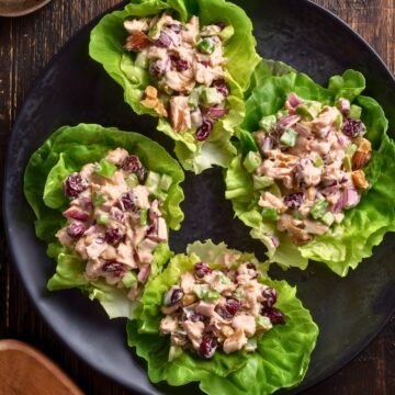Overhead view of four Cranberry Walnut Chicken Lettuce Wraps filled with creamy chicken salad, dried cranberries, celery, red onion, and walnuts on a black plate.