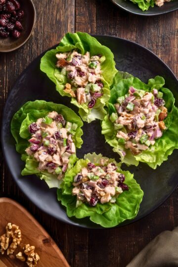 Overhead view of four Cranberry Walnut Chicken Lettuce Wraps filled with creamy chicken salad, dried cranberries, celery, red onion, and walnuts on a black plate.