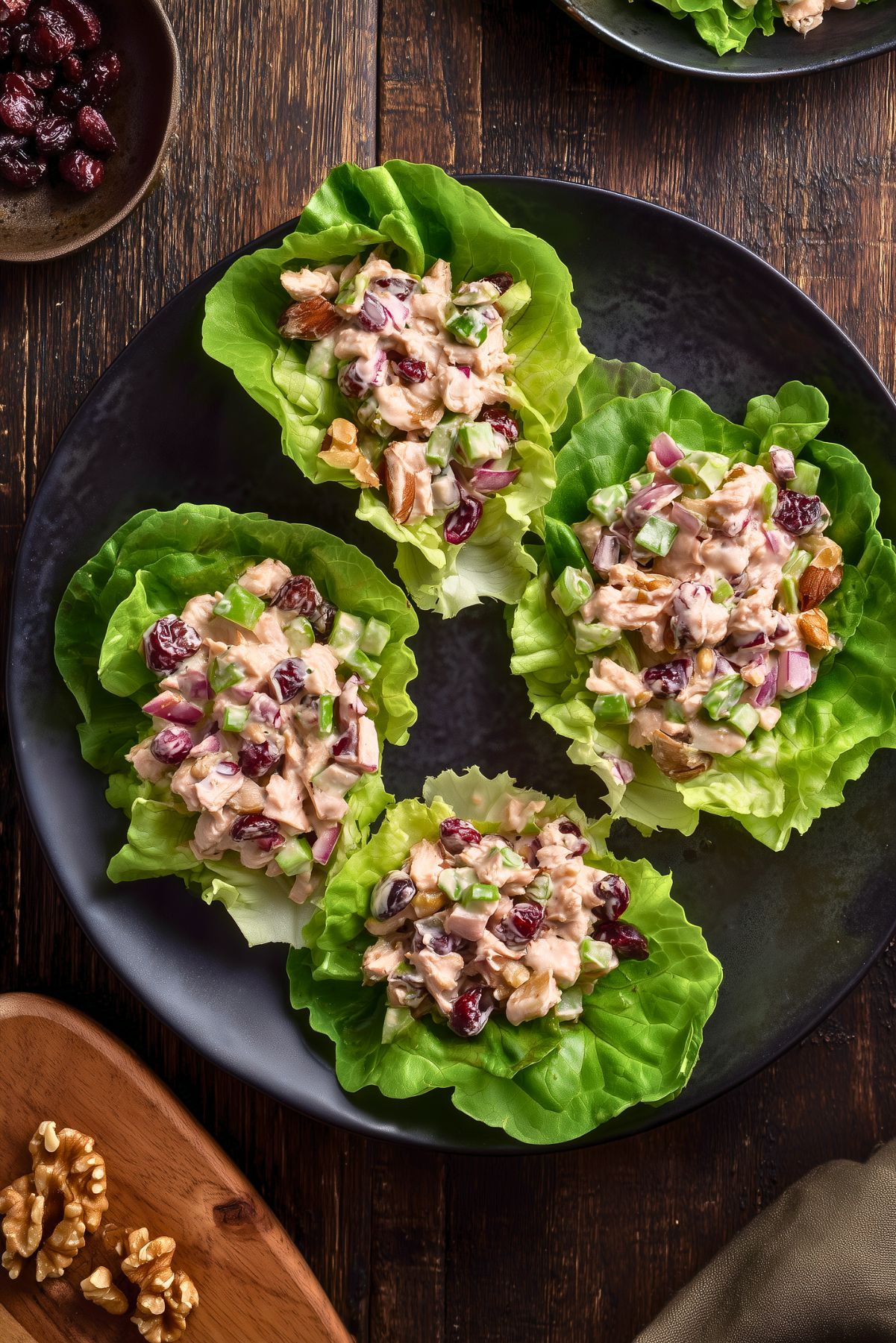Overhead view of four Cranberry Walnut Chicken Lettuce Wraps filled with creamy chicken salad, dried cranberries, celery, red onion, and walnuts on a black plate.