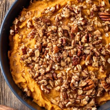 Overhead view of Healthy Slow Cooker Sweet Potato Casserole with creamy mashed sweet potatoes topped with chopped pecans, oats, and warm spices in a black bowl.