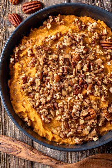 Overhead view of Healthy Slow Cooker Sweet Potato Casserole with creamy mashed sweet potatoes topped with chopped pecans, oats, and warm spices in a black bowl.
