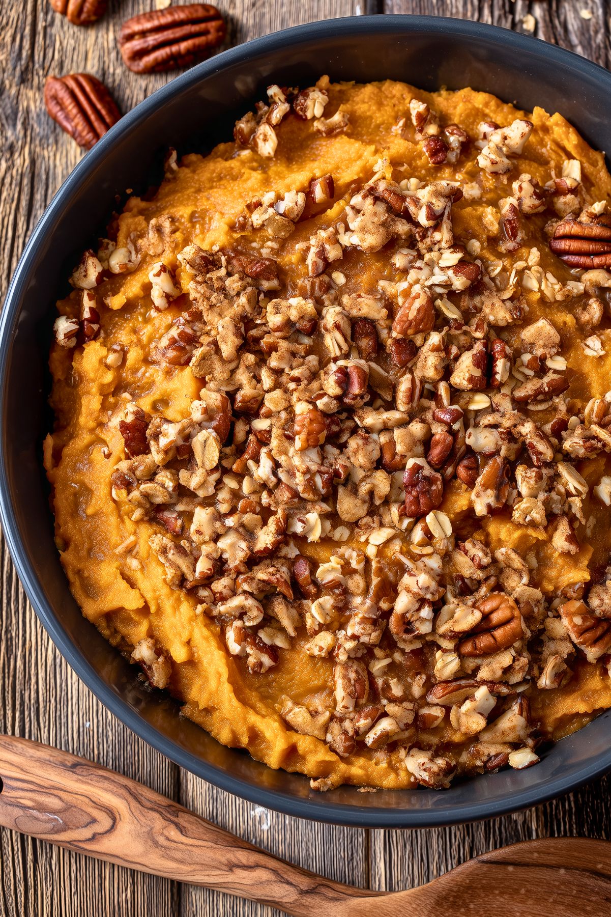 Overhead view of Healthy Slow Cooker Sweet Potato Casserole with creamy mashed sweet potatoes topped with chopped pecans, oats, and warm spices in a black bowl.