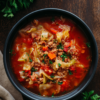 Overhead view of high protein cabbage roll soup with ground turkey, tender cabbage, carrots, and tomatoes in a black bowl on rustic wood.