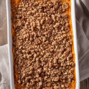 Overhead view of maple pecan sweet potato casserole in a white baking dish, with orange sweet potato filling covered in a generous brown sugar pecan crumble topping.