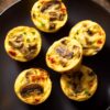 Mushroom and roasted red pepper egg bites with browned mushrooms, red pepper pieces, and green onion on a matte black plate.