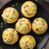 Six roast beef and cheddar egg bites with melted cheddar and green onions arranged on a black plate over a rustic wood table.