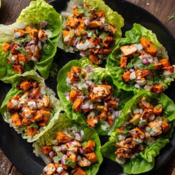 Overhead view of roasted sweet potato chicken lettuce wraps topped with red onion, cilantro, and creamy herb sauce on a matte black plate.