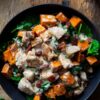 Overhead view of a Tuscan chicken sweet potato bowl with roasted sweet potatoes, chicken, spinach, bacon, and creamy sauce in a black bowl on a rustic wood table.