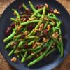 Overhead view of cranberry pecan green beans with dried cranberries and chopped pecans on a black plate over a rustic wood table.