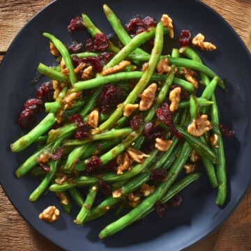 Overhead view of cranberry pecan green beans with dried cranberries and chopped pecans on a black plate over a rustic wood table.