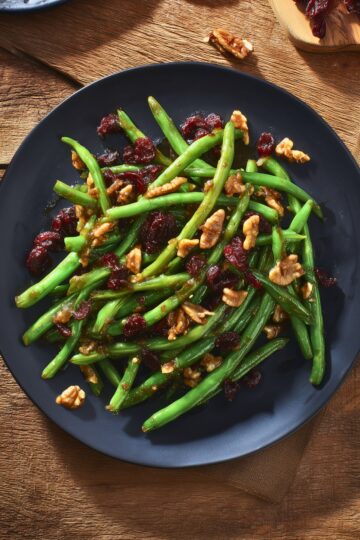 Overhead view of cranberry pecan green beans with dried cranberries and chopped pecans on a black plate over a rustic wood table.