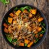 Overhead view of a French Onion Beef Sweet Potato Bowl filled with seasoned ground beef, golden caramelized onions, roasted sweet potato cubes, fresh spinach, and shredded cheese. Served in a matte black bowl on a rustic wooden table.