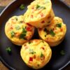Close-up of four homemade Pico de Gallo Egg Bites with diced tomatoes, peppers, melted cheese, and fresh cilantro on a black plate.