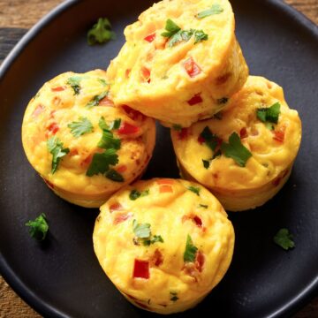 Close-up of four homemade Pico de Gallo Egg Bites with diced tomatoes, peppers, melted cheese, and fresh cilantro on a black plate.