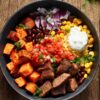 Overhead view of a steak burrito sweet potato bowl with browned steak pieces, roasted sweet potato cubes, black beans, corn, diced red onion, fresh salsa, shredded cheese, sour cream, and cilantro in a matte black bowl on rustic wooden planks.