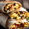 Close-up of three stacked Tex-Mex breakfast burrito halves on a black plate. Golden toasted flour tortillas are filled with fluffy scrambled eggs, black beans, sweet corn, red bell peppers, and melted cheese. The colorful fillings are visible in each cut end.