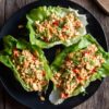 Three Thai peanut chicken lettuce wraps on a black plate, filled with ground chicken, creamy peanut sauce, red peppers, chopped peanuts, green onions, and cilantro.